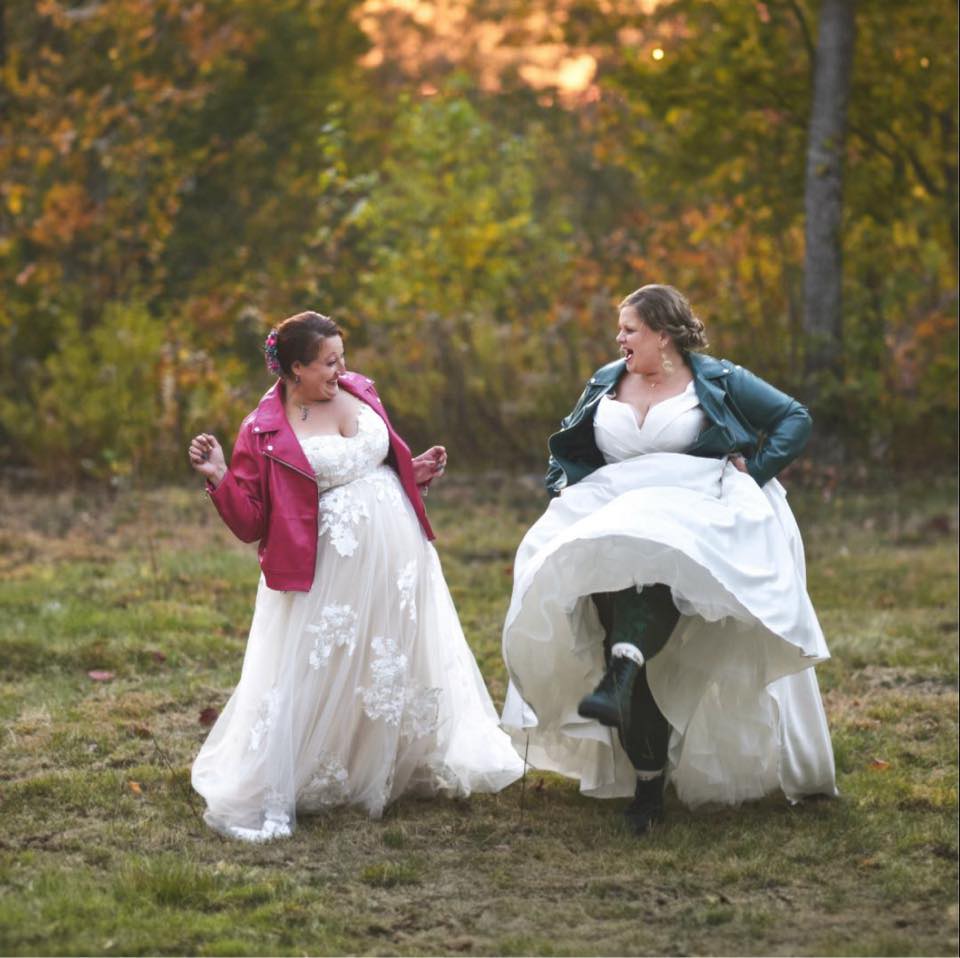 Two brides laughing and dancing in a field